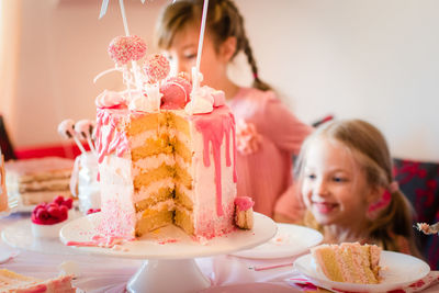 Close-up of birthday cake on decorated table with siblings in background