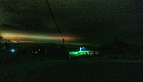 Illuminated street lights on field against sky at night