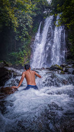 Rear view of shirtless man splashing water