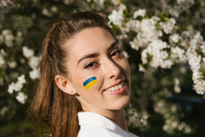 Outdoor portrait of ukrainian woman with blue and yellow ukrainian flag on her cheek on cherry