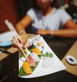 Midsection of young girl holding sushi on table in restaurant