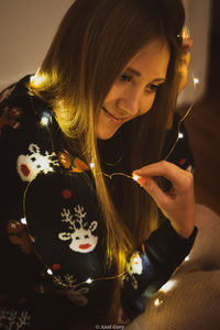 Close-up of young woman with illuminated string lights at home