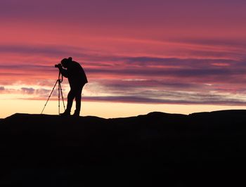 Silhouette man photographing against sky during sunset