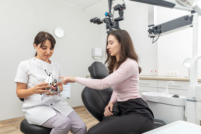 Dentist holding dental articulator with dental gypsum prosthesis model showing it to a patient