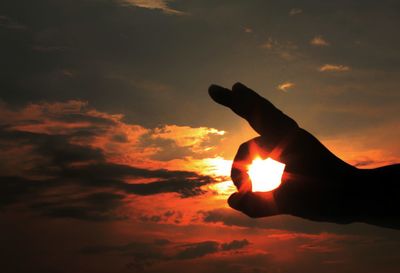 Silhouette person hand against orange sunset sky