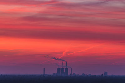 Silhouette factories in city against dramatic sky during sunset