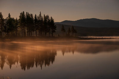 Scenic view of lake by silhouette trees against sky