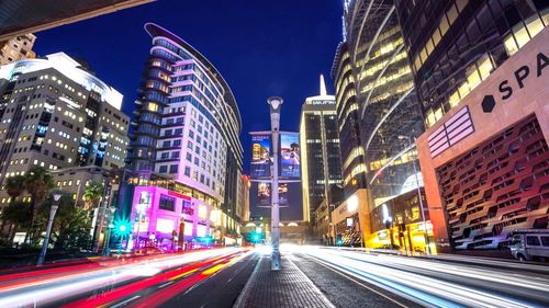 Light trails on city street amidst buildings at night