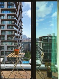 Buildings in city against sky seen through glass window