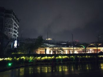 Illuminated buildings by river against sky at night