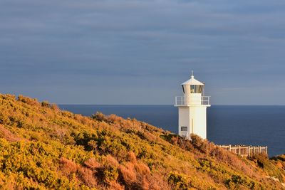 Lighthouse amidst sea and buildings against sky