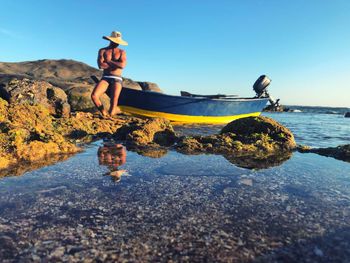 Full length of man on rock at beach against clear sky