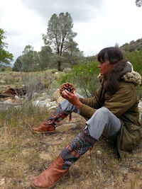 Woman holding pine cone on field against sky