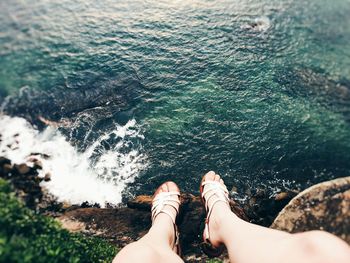 Low section of woman dangling legs over sea