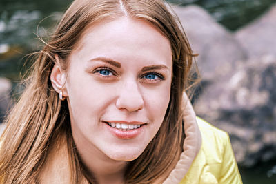 Portrait of young attractive blue-eyed woman looking at camera and smiling in yellow jacket outdoors