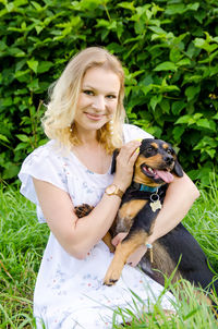 Portrait of young woman embracing with dog while sitting outdoors