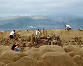 People building sandcastle against sky