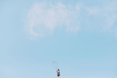Distant view of woman standing on rock against blue sky