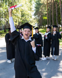 Portrait of woman wearing graduation gown standing in city