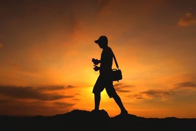 Side view of silhouette man walking on field at sunset