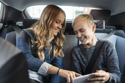 Smiling siblings using phone while sitting in car