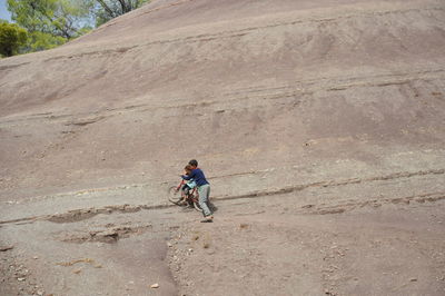 Boy assisting sister riding bicycle on hill