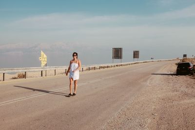 Full length of young woman walking on bridge against sky