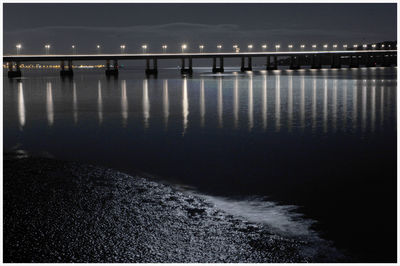 Illuminated bridge over river against sky at night