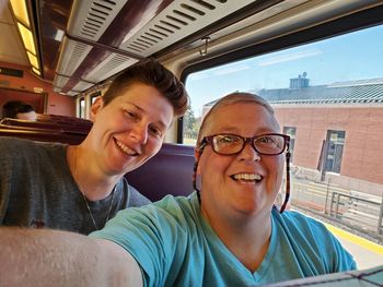 Portrait of smiling couple sitting by window in train