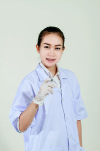 Portrait of smiling young doctor with syringe standing over gray background