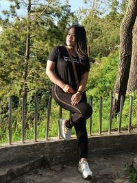 Full length of woman standing on railing against trees