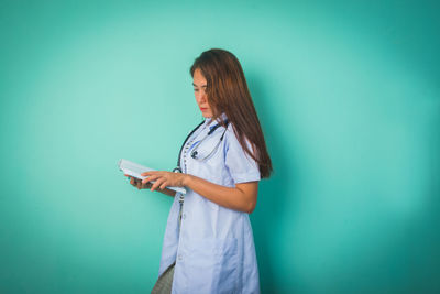 Woman holding smart phone while standing against wall