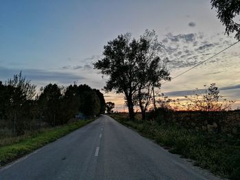 Road amidst trees on field against sky