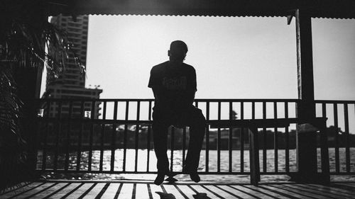 Rear view of silhouette man standing against railing in city