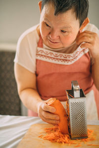 Lifestyle, education. an elderly woman with down syndrome rubs carrots on a grater