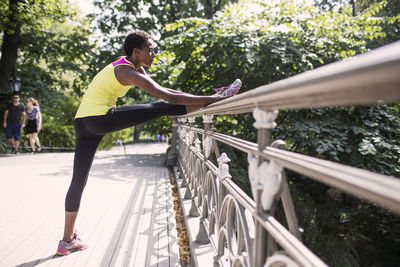 Woman practicing stretching exercise by railing at park