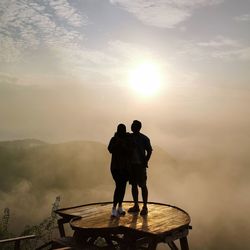 Rear view of silhouette friends standing on mountain against sky