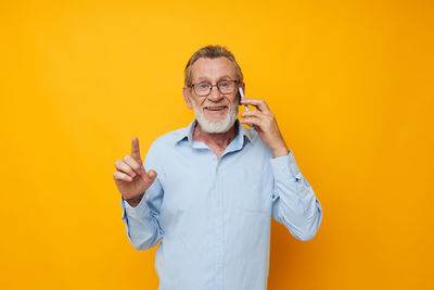 Portrait of senior man talking on phone against yellow background