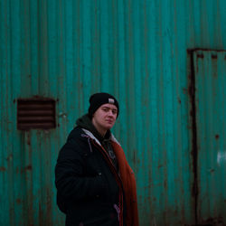 Young man in warm clothes standing against corrugated iron