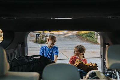 Smiling brothers loading luggage in trunk seen through car