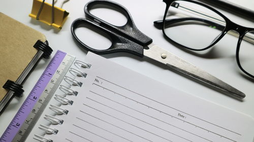 High angle view of scissors and eyeglasses with ruler on book