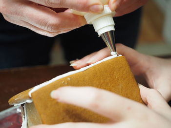 Adding icing to ginger bread house, closeup of girls hands.