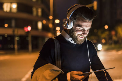 Smiling young man with tablet and headphones on urban street at night