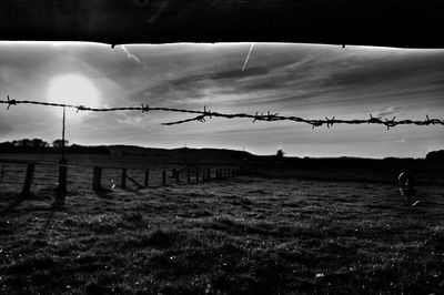 Silhouette of barbed wire fence on field against sky