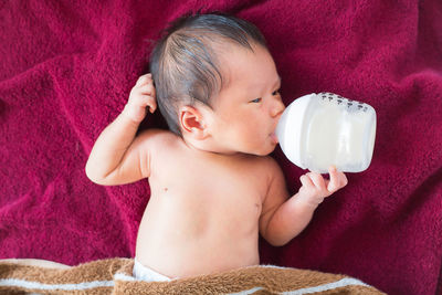 High angle view of baby with milk bottle lying on bed