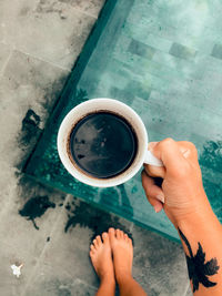 Low section of person holding coffee cup on floor