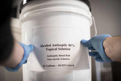 A distiller puts the label on a bucket of hand sanitizer.