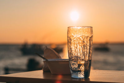 Close-up of drink in glass on table against sea during sunset