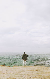 Rear view of man standing on shore at beach against sky