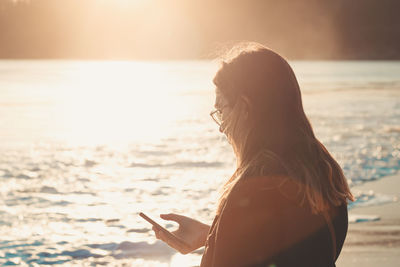 Young woman using mobile phone while standing on beach